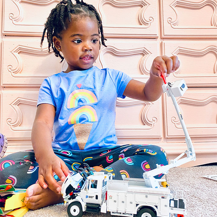 A toddler girl sits on the ground playing with a toy Dominion Energy bucket truck