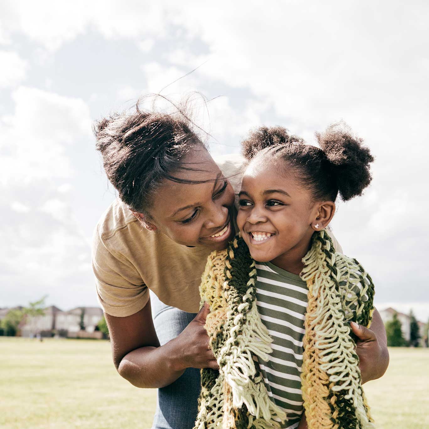 A mother hugs her child from behind while outside