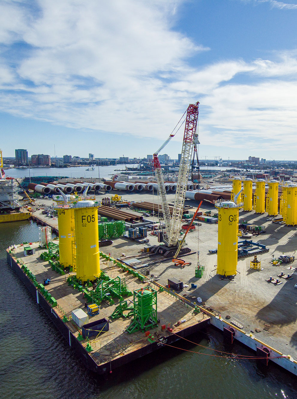 Components for turbine installation are staged at Portsmouth Marine Terminal, with the coast of Norfolk in the background
